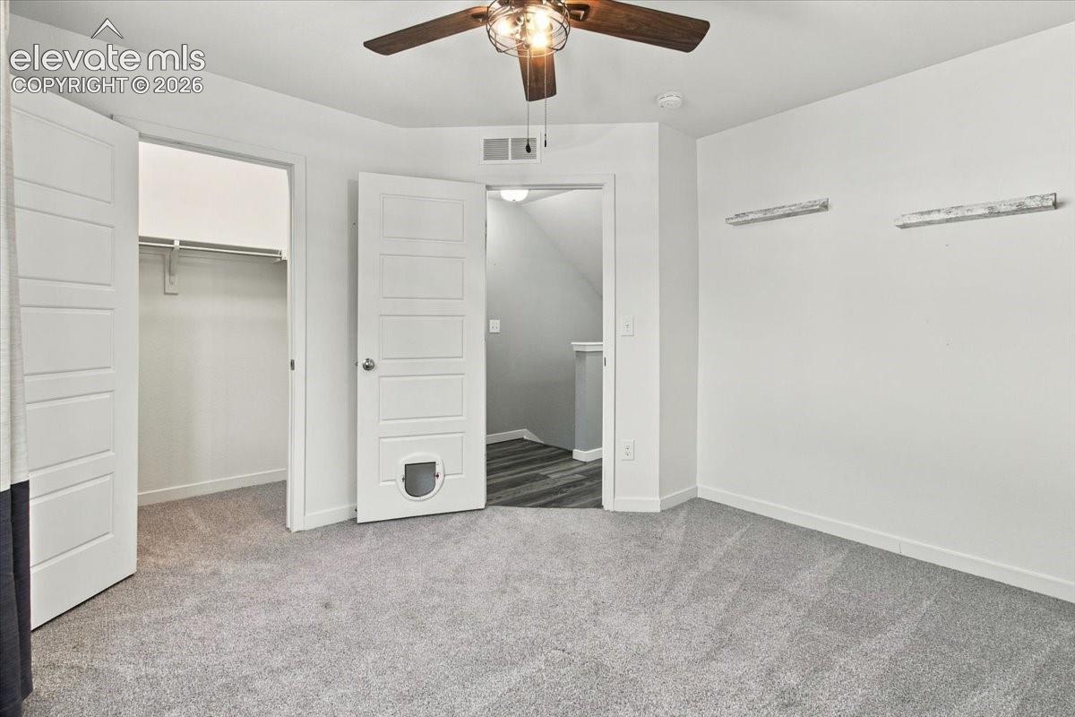 Carpeted flooring, ceiling fan, white paneled doors, and a built-in closet with shelving