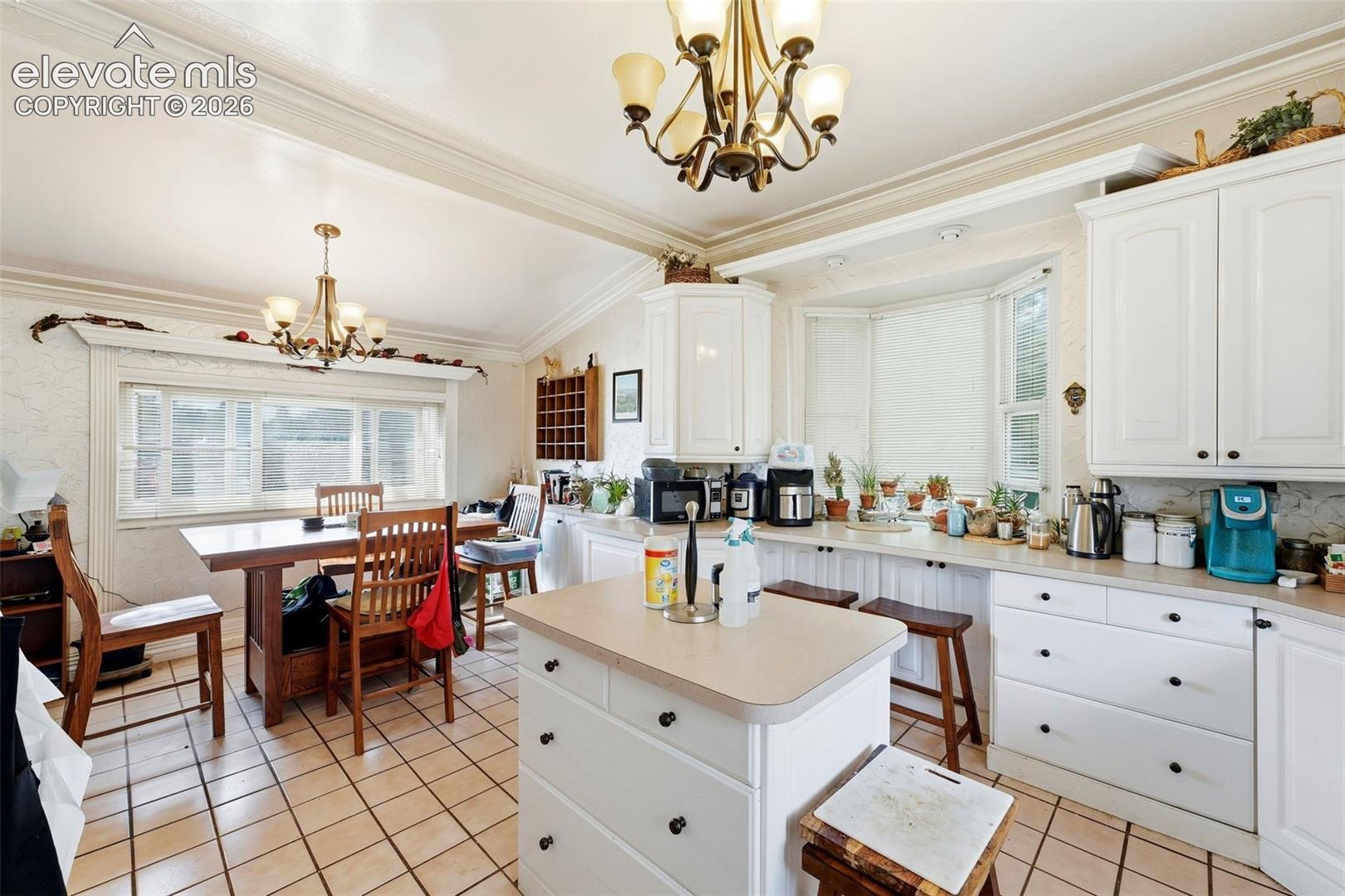 White cabinetry with black hardware, bay window, tile flooring, and a central island with built-in storage