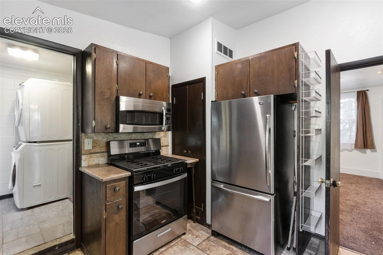 Kitchen featuring stained wood cabinetry, stainless steel appliances, a built-in microwave, stone-surface countertops, and a full-height utility storage cabinet