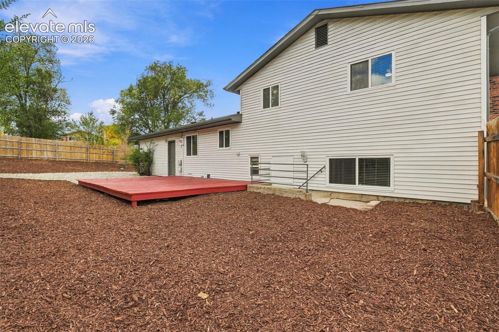 Exterior rear elevation featuring horizontal siding, a red-painted wood deck, metal safety railing, and a fenced perimeter