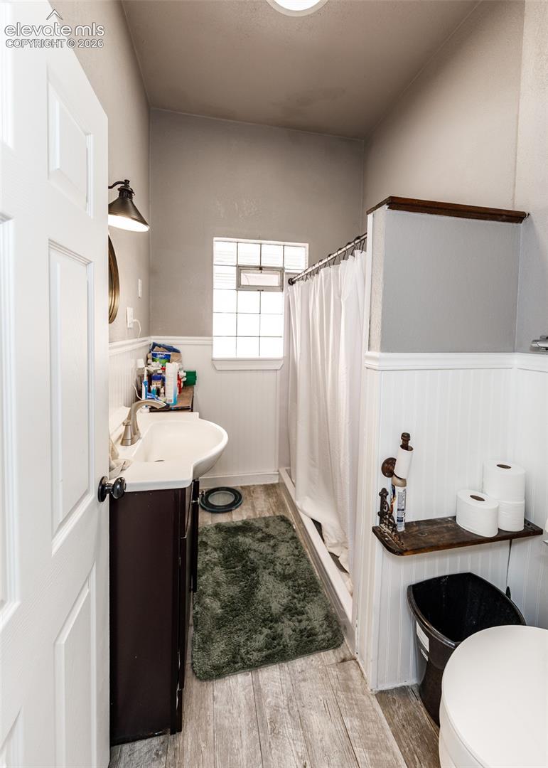 Bathroom featuring a dark wood finish vanity with a white basin sink, wood-finish flooring, a shower with a white curtain, and a glass block window