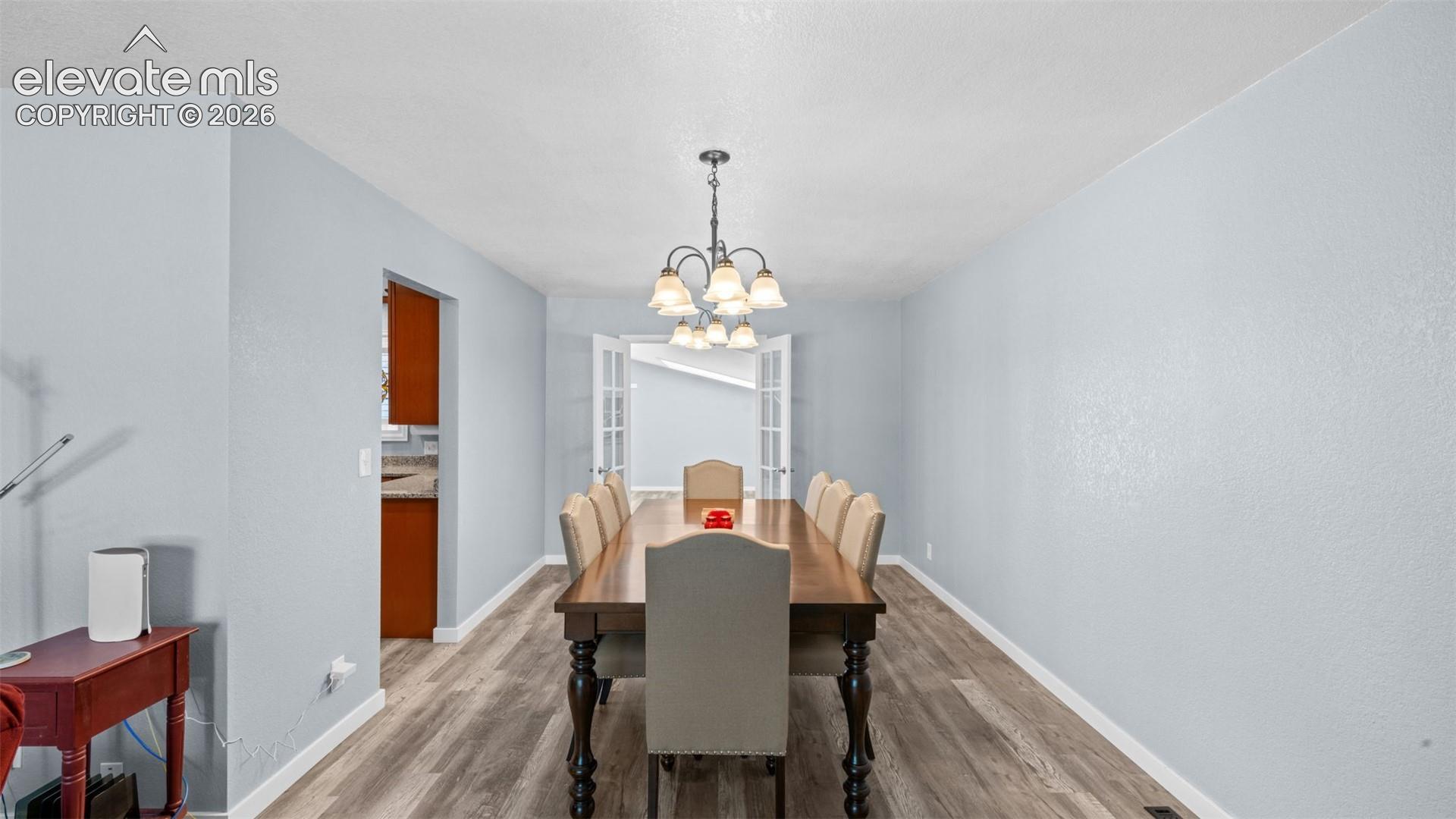 Spacious dining area featuring wood-finish flooring, light blue wall finishes, and a traditional chandelier