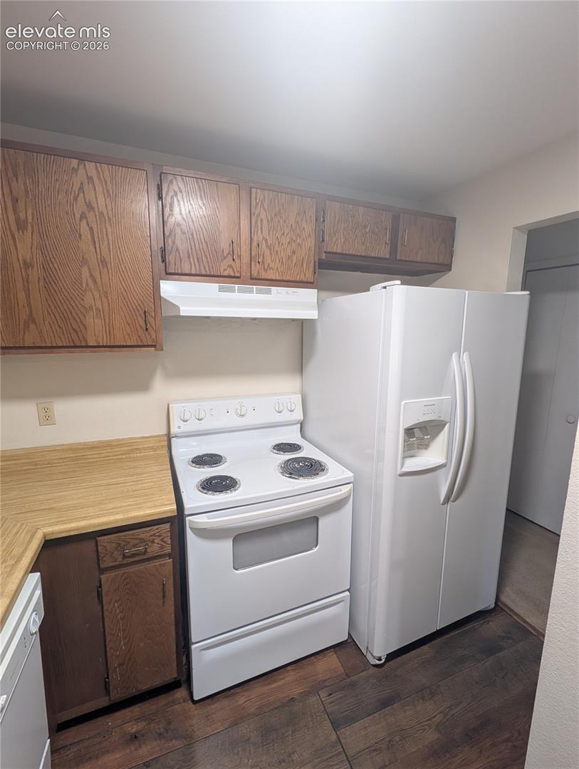 Kitchen featuring wood-finish flooring, wood cabinetry, light-toned countertops, white range, and a white side-by-side refrigerator