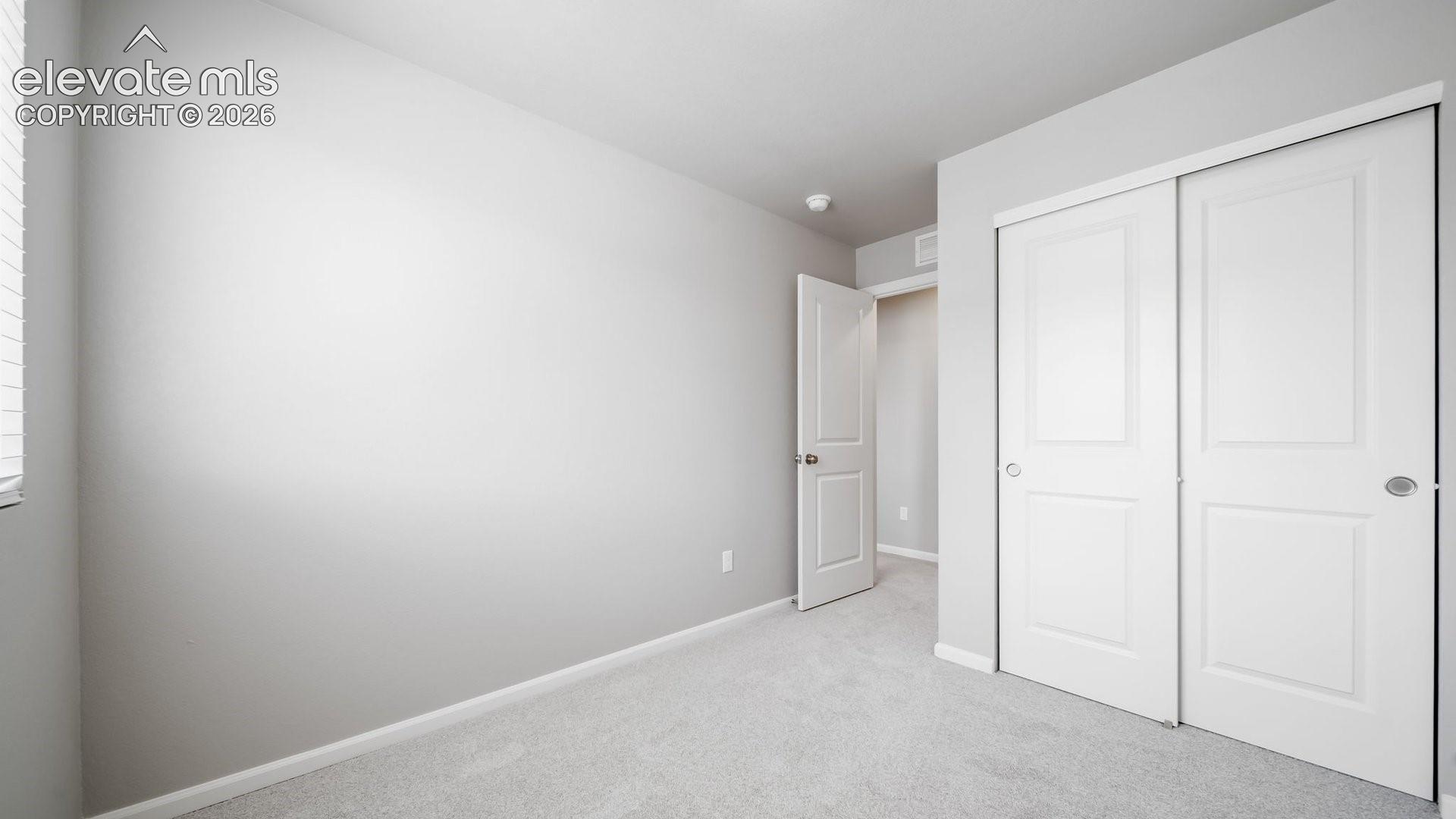 Room featuring neutral wall tones, carpeted flooring, a sliding closet with panel doors, and a paneled interior door with metal hardware
*photos of a model home*