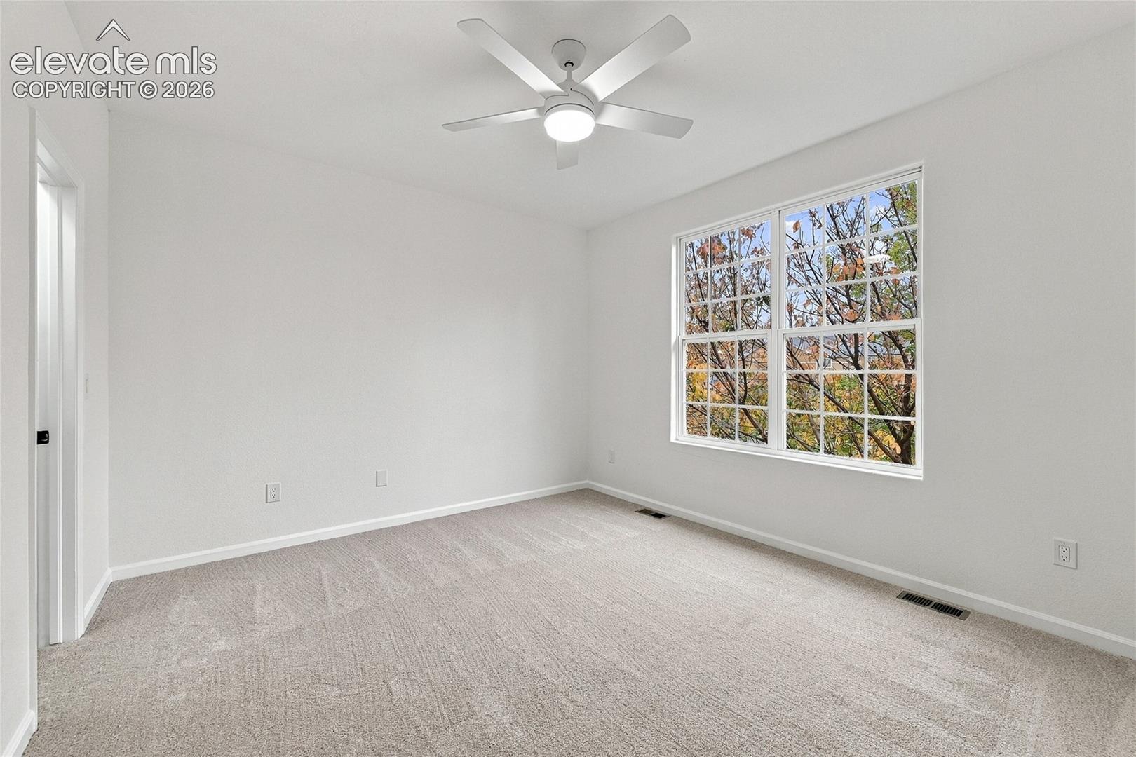Neutral wall palette featuring carpeting, a multi-pane window, and a ceiling fan with integrated lighting