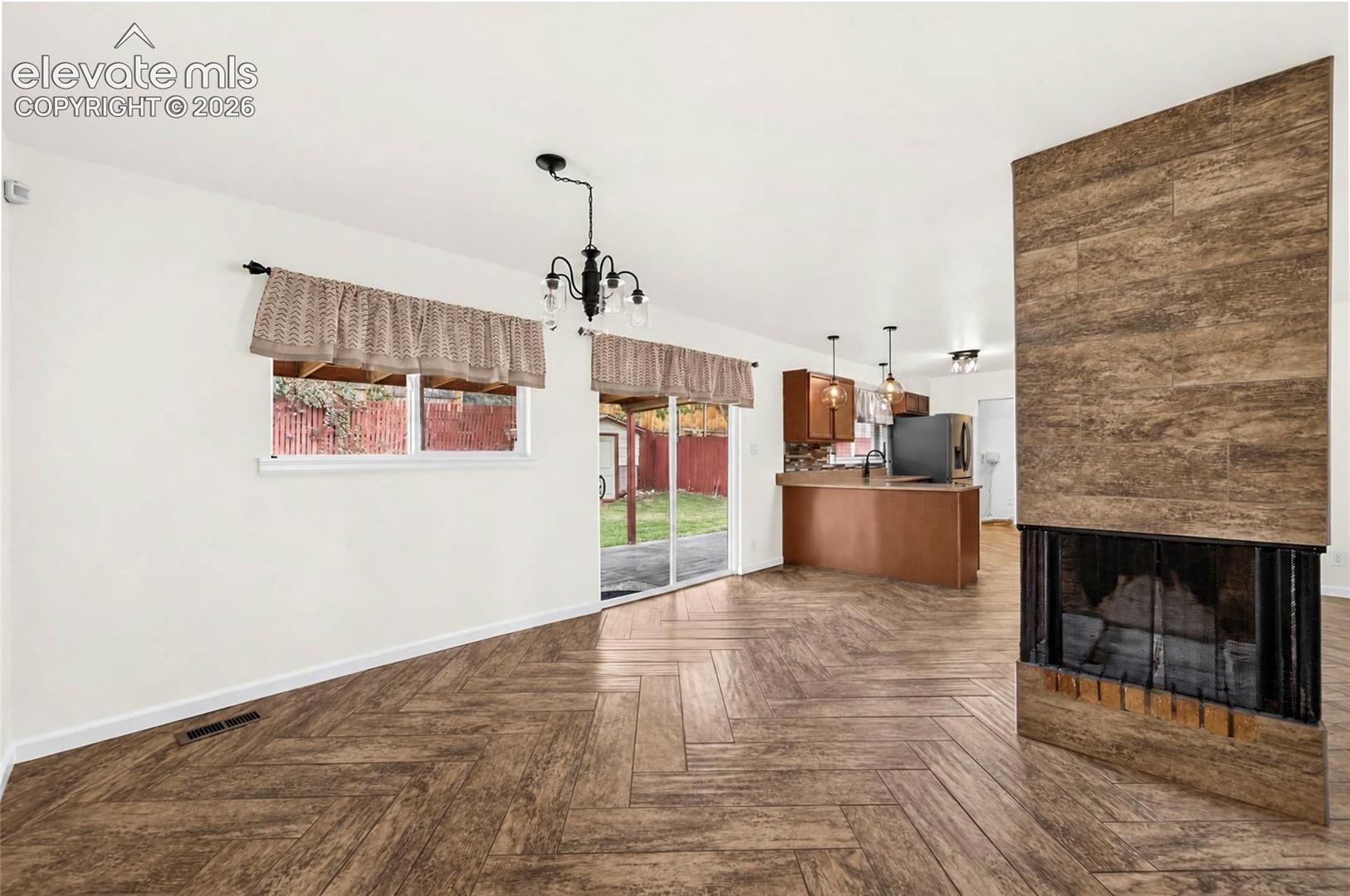 Floor-to-ceiling fireplace surround with wood-finish tile, herringbone-patterned wood-finish flooring, sliding glass door, and multi-arm chandelier lighting
