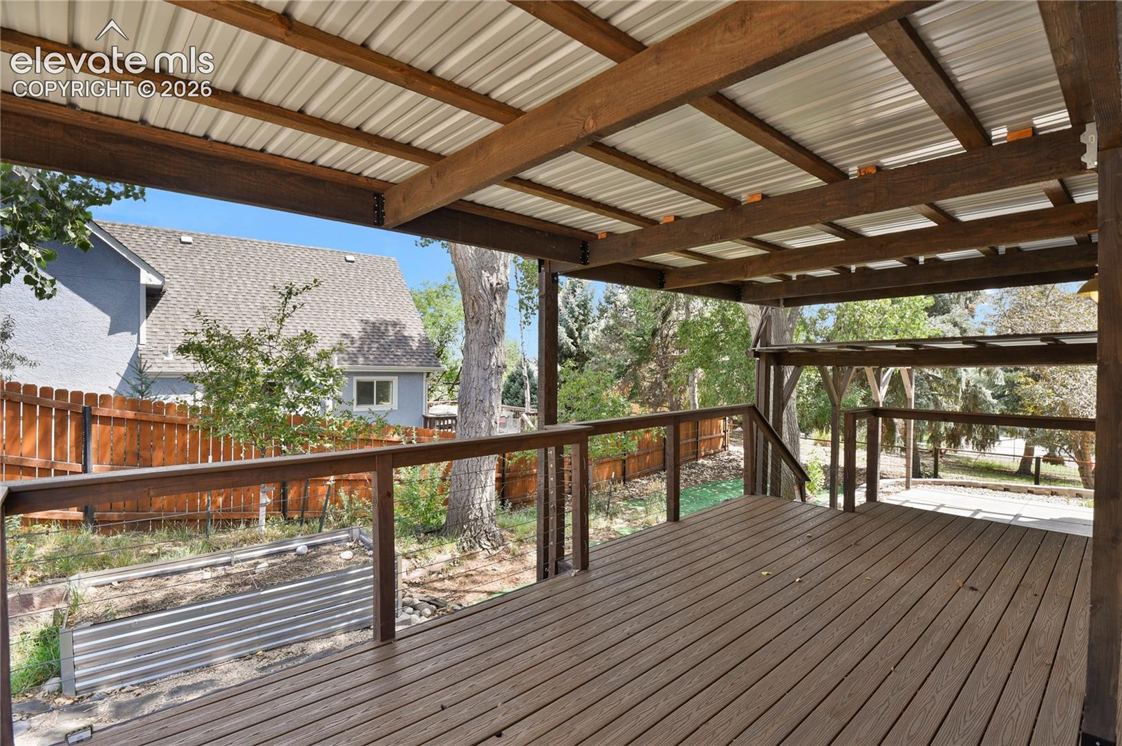 Covered deck featuring composite decking, exposed timber framing, a metal roof, and a wooden railing