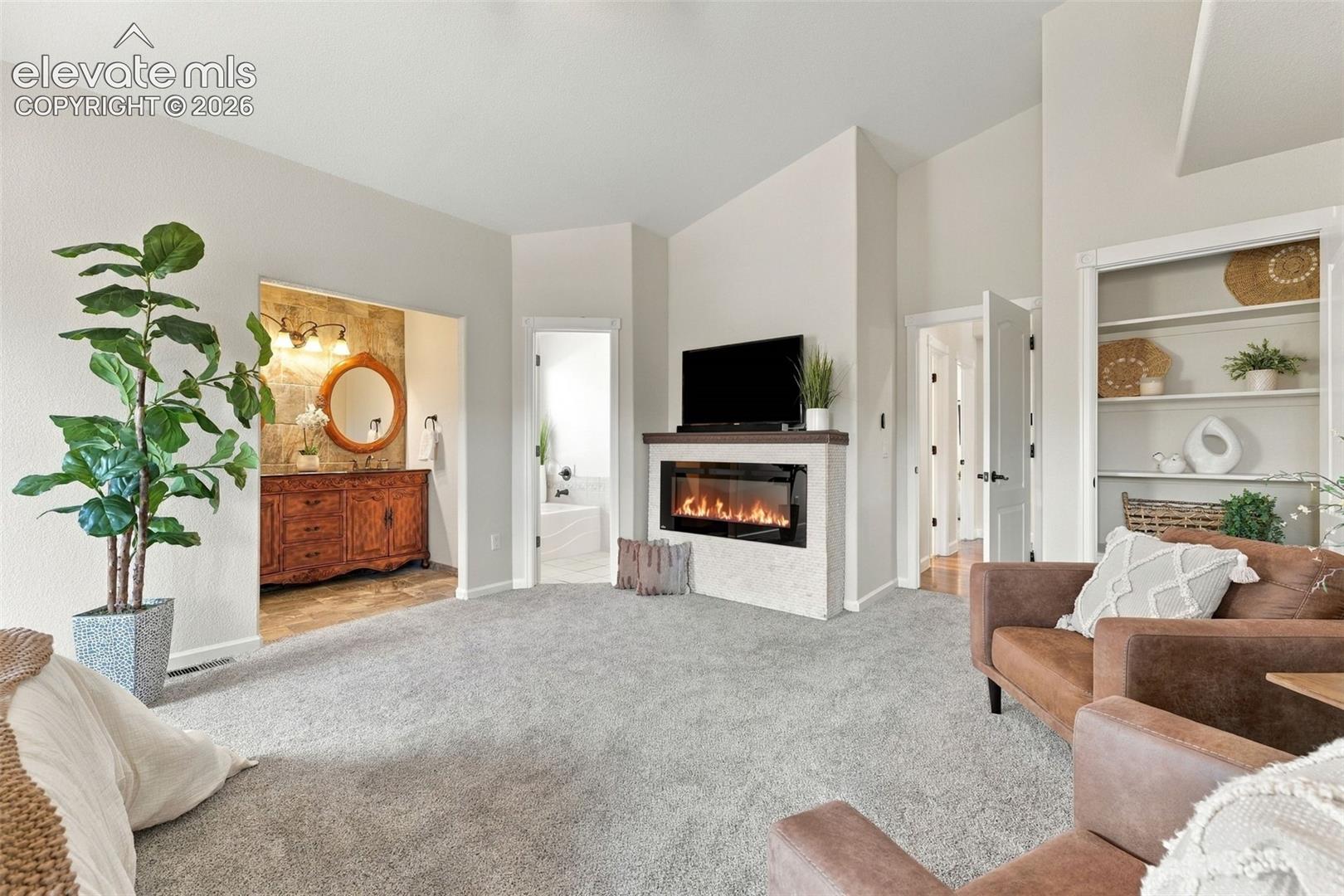 Vaulted ceilings, a built-in electric fireplace with stone surround, custom wood cabinetry in the vanity area, and recessed shelving