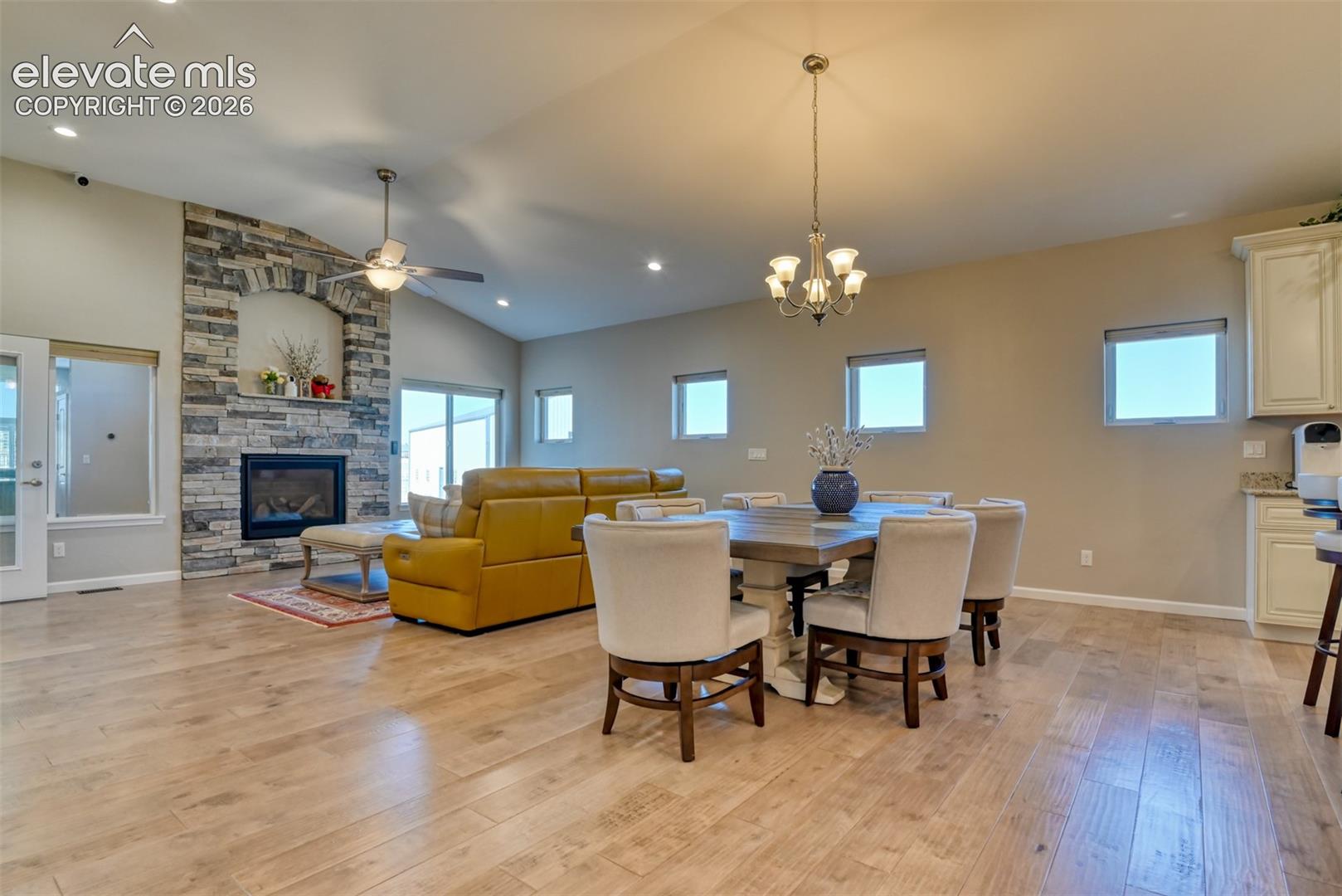 Vaulted ceilings, wood-finish flooring, stone-clad fireplace, recessed lighting, and a chandelier-lit dining area.
