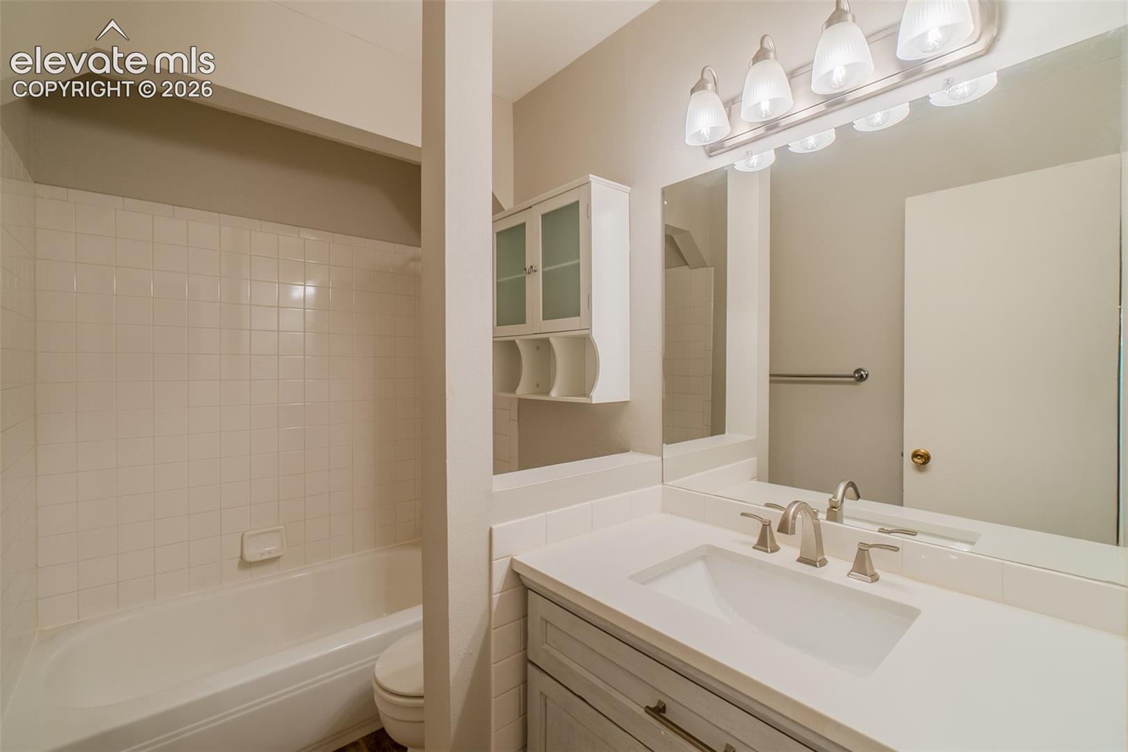 Bathroom featuring a single vanity with an integrated sink, broad mirror, and overhead four-light fixture