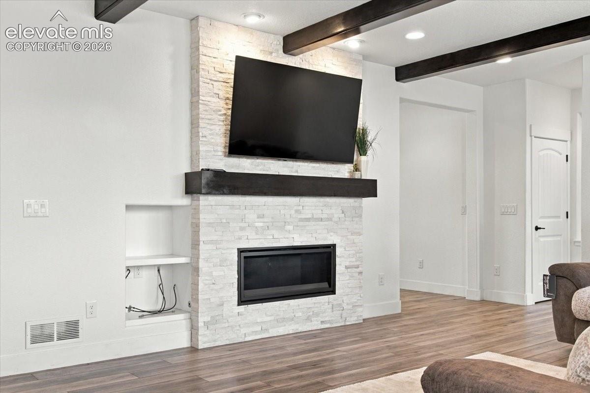 Floor-to-ceiling stacked stone fireplace featuring a dark timber mantel and built-in shelving, complemented by exposed decorative ceiling beams and wood-finish flooring