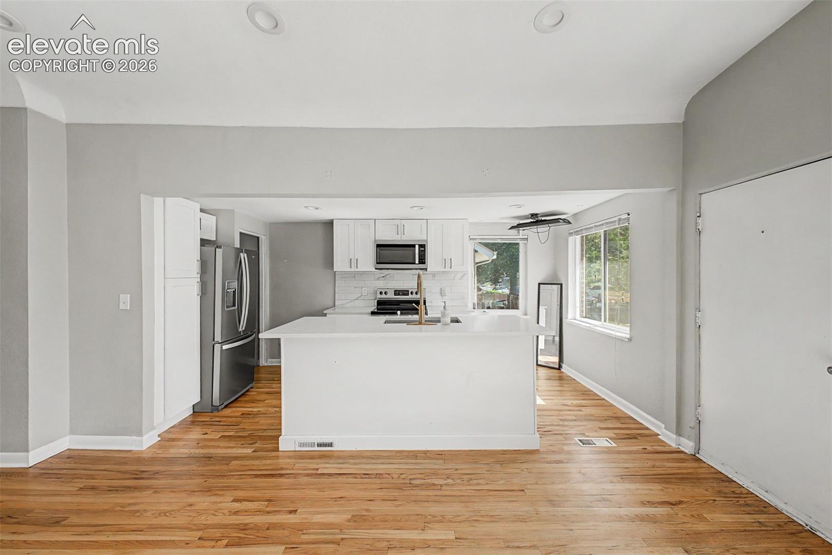 Modern kitchen featuring an island with an undermount sink and brass faucet, white shaker cabinetry, stainless steel appliances, and a subway tile backsplash