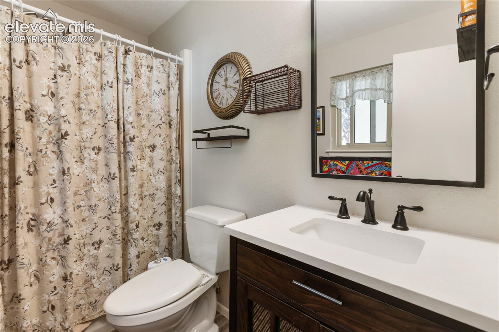 White countertop with an integrated rectangular sink, bronze-finish faucet, and a dark wood-finish vanity