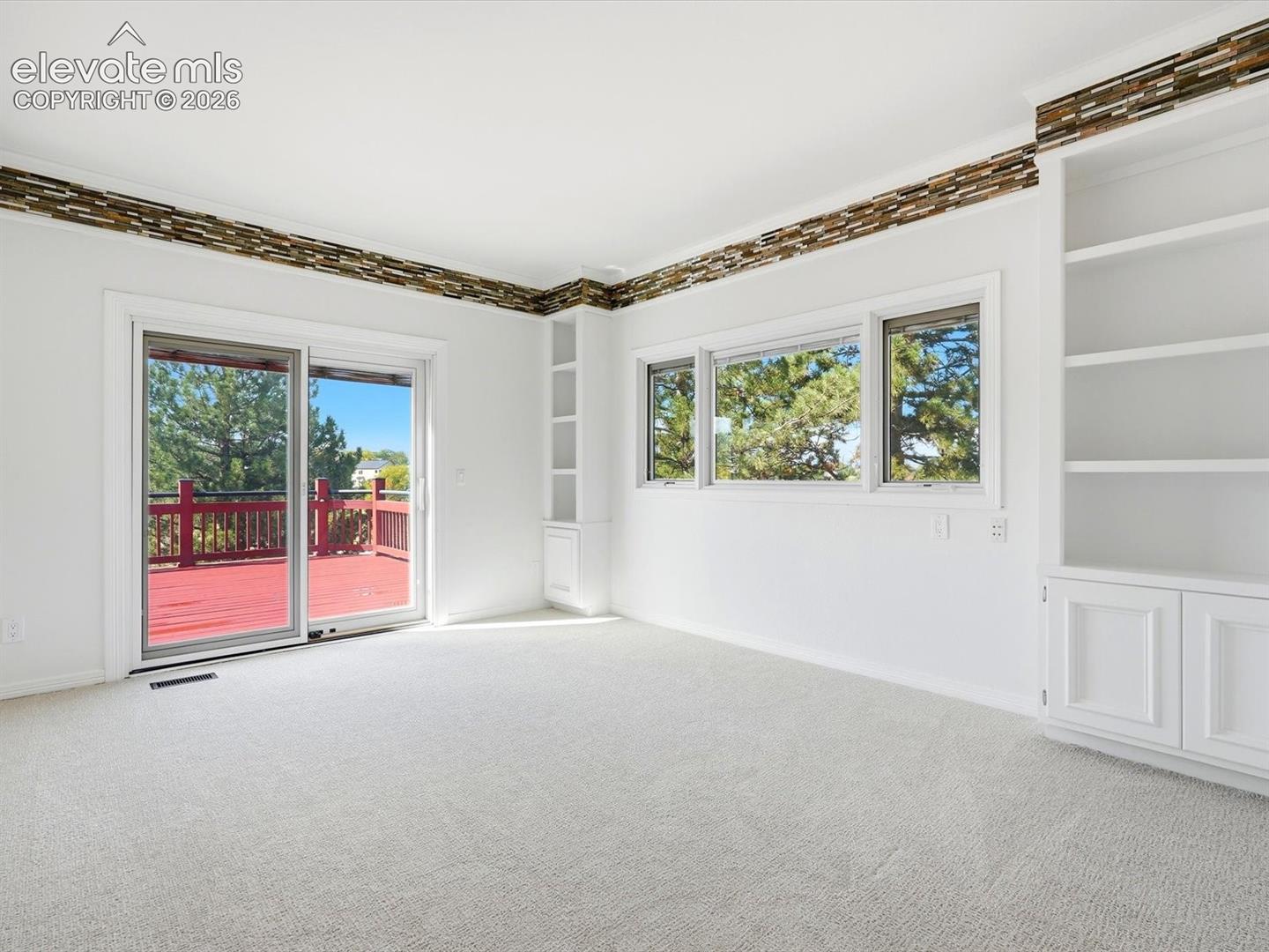 Interior space featuring built-in floor-to-ceiling shelving, stone-tiled crown molding, sliding glass doors, and a multi-pane window configuration