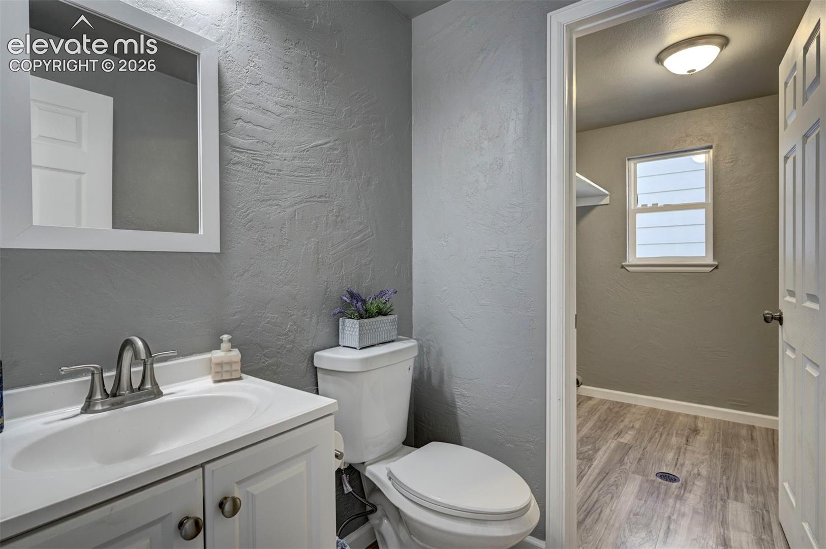 Bathroom featuring a white vanity cabinet, integrated sink with a dual-handle faucet, framed wall mirror, and wood-finish flooring
