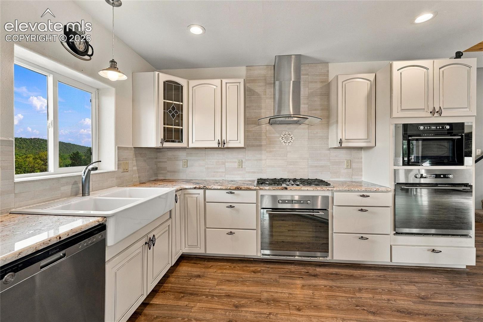Kitchen featuring off-white cabinetry, stone-finish countertops, stainless steel appliances, a white farmhouse sink, and wood-finish flooring