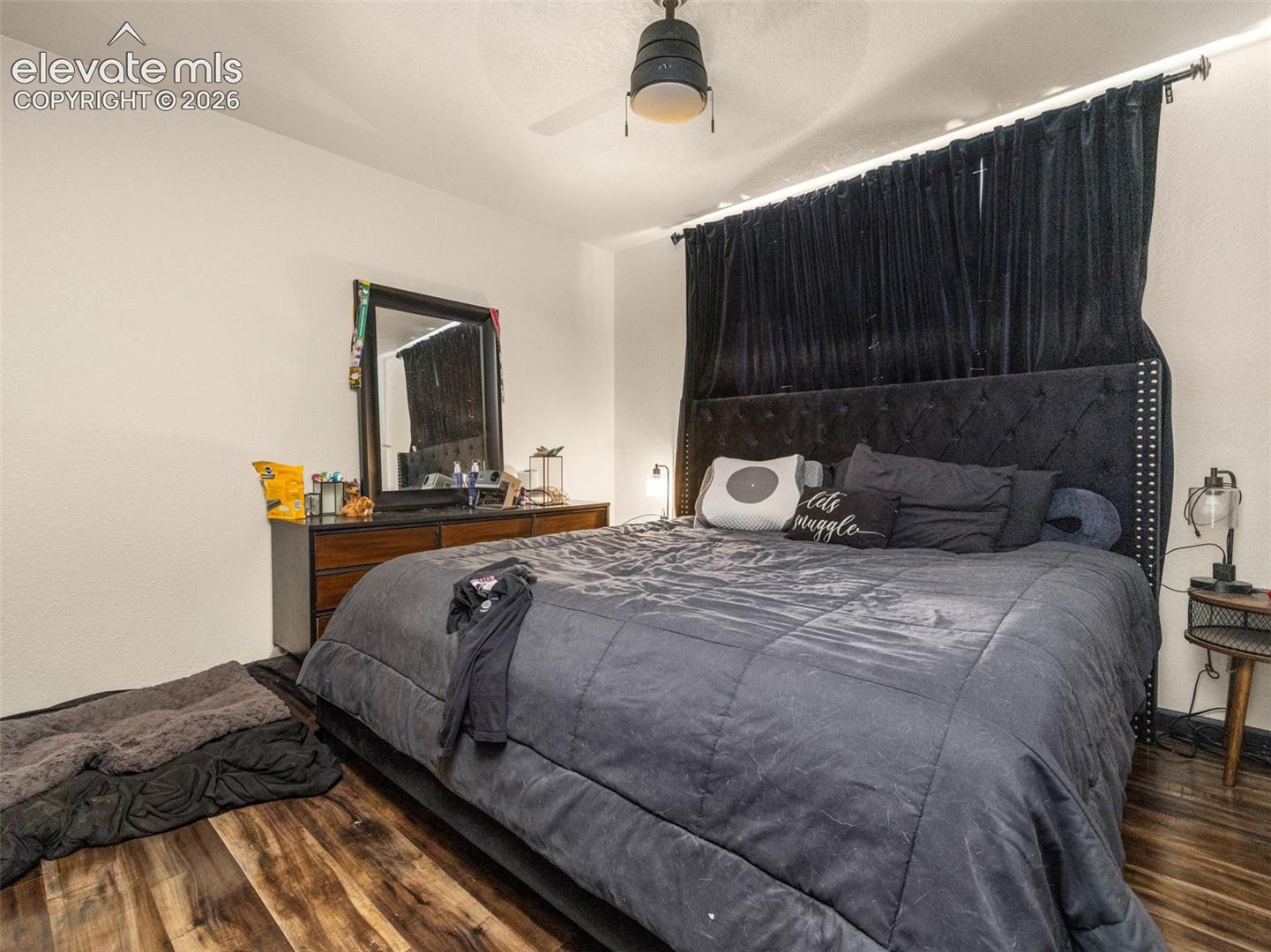 Wood-finish flooring, ceiling fan with integrated lighting, and a dark wood-tone dresser with a mirror