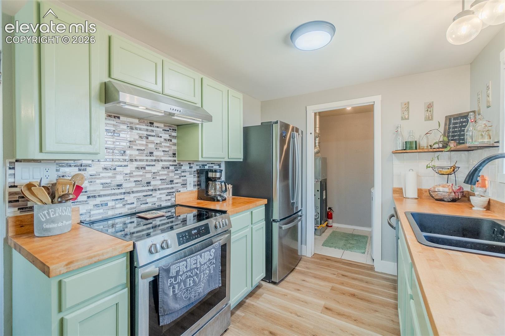 Kitchen featuring light green cabinetry, wood-finish countertops, and a mosaic tile backsplash