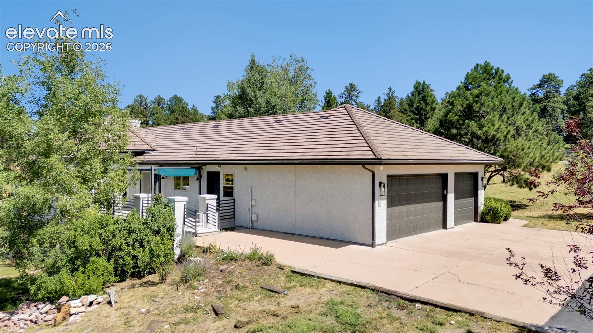 Stucco exterior with a tiled hip roof, featuring a two-car garage with dark paneled doors and an exposed aggregate concrete driveway