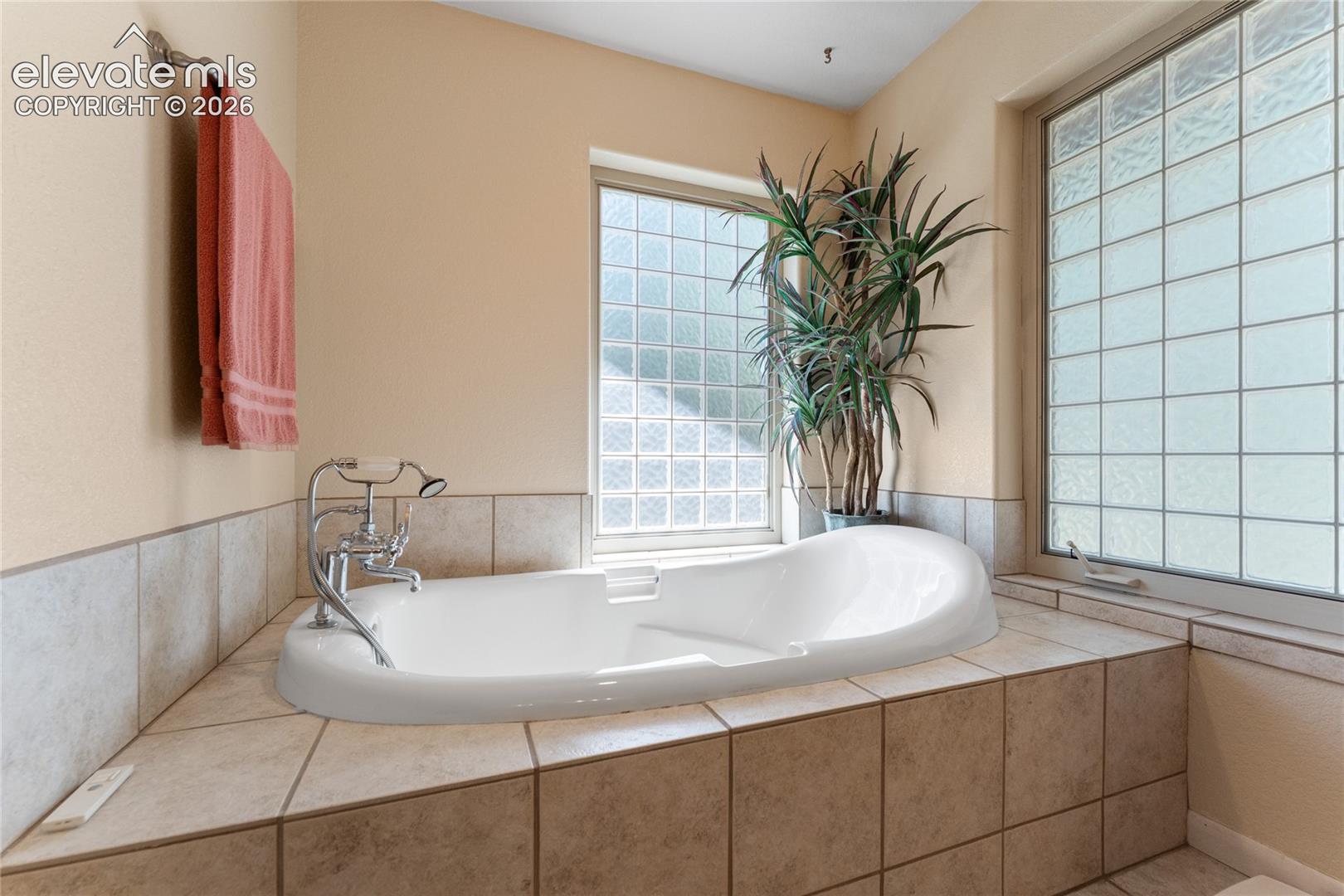Soaking tub set within a tiled surround, featuring a chrome faucet with a handheld sprayer