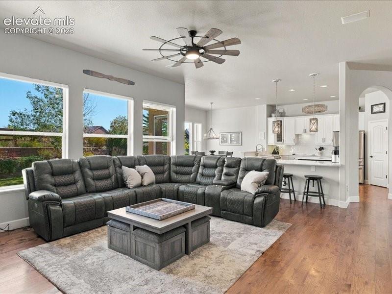 Open-concept living space featuring a sectional reclining sofa, wood-finish flooring throughout, and abundant natural light from expansive windows