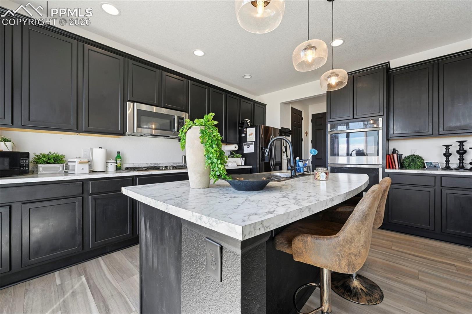 Kitchen featuring dark cabinetry, stainless steel appliances, a center island with seating, pendant lighting, and wood-finish flooring