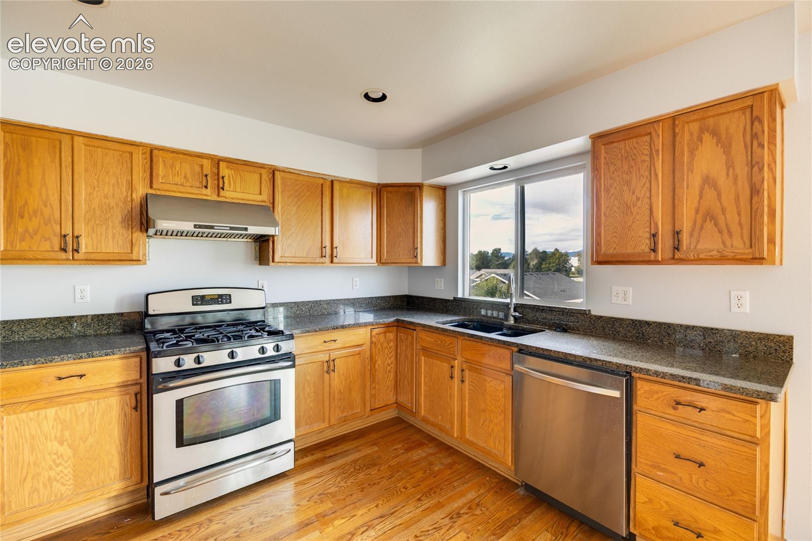 Kitchen featuring wood cabinetry, dark countertops, stainless steel appliances, and wood-finish flooring