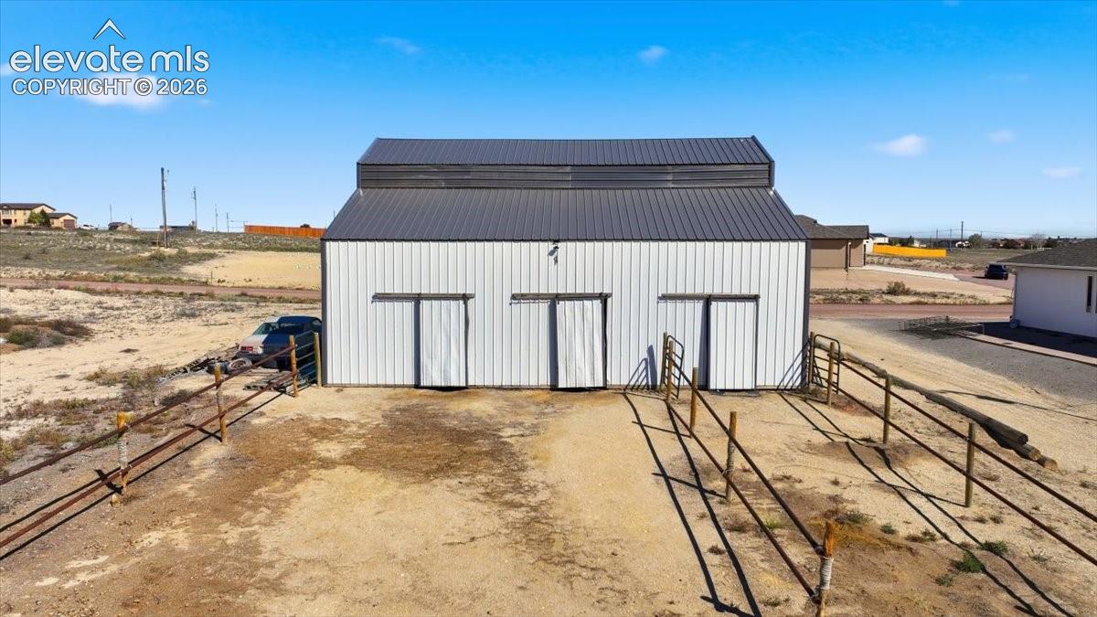 Detached metal barn featuring vertical siding, a dark metal roof, and three sliding access doors, complemented by external perimeter fencing