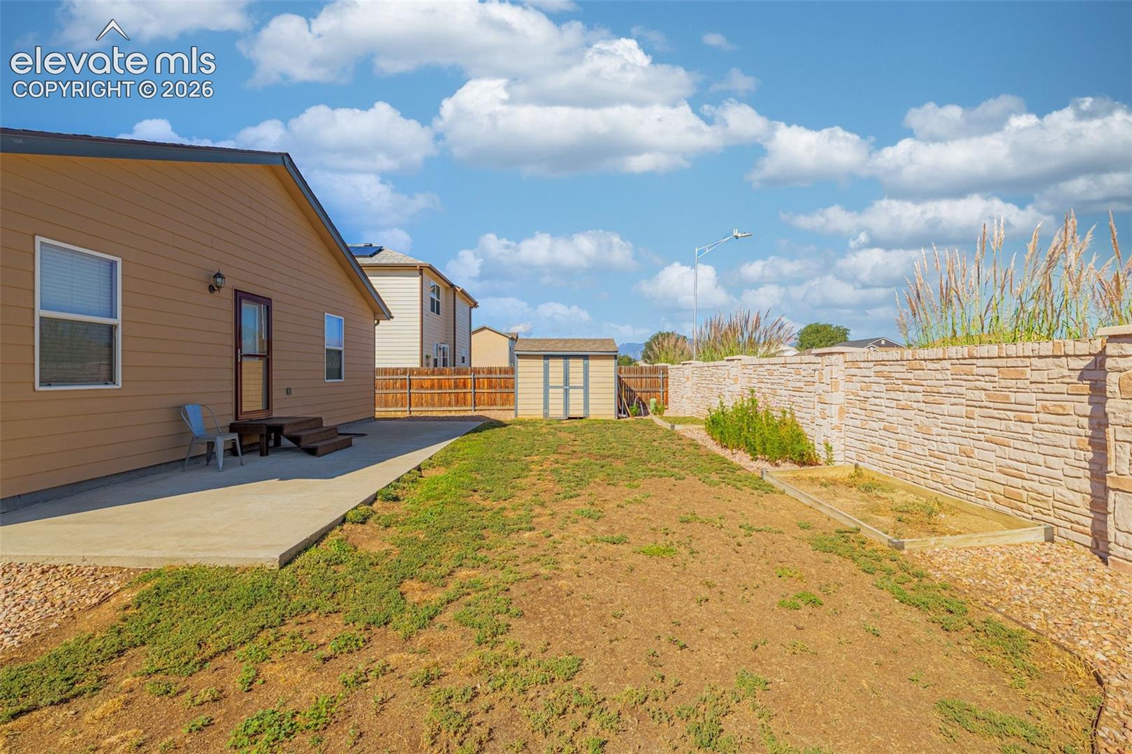 Private backyard featuring a concrete patio, exterior access, a storage shed, and a stone wall