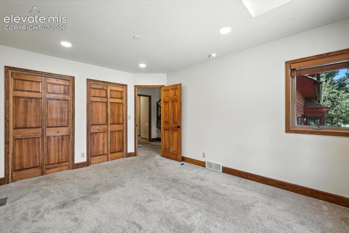 Interior room featuring wood-finish door frames, two sets of built-in wood-finish bifold closet doors, recessed lighting, and a single window with wood-finish casing