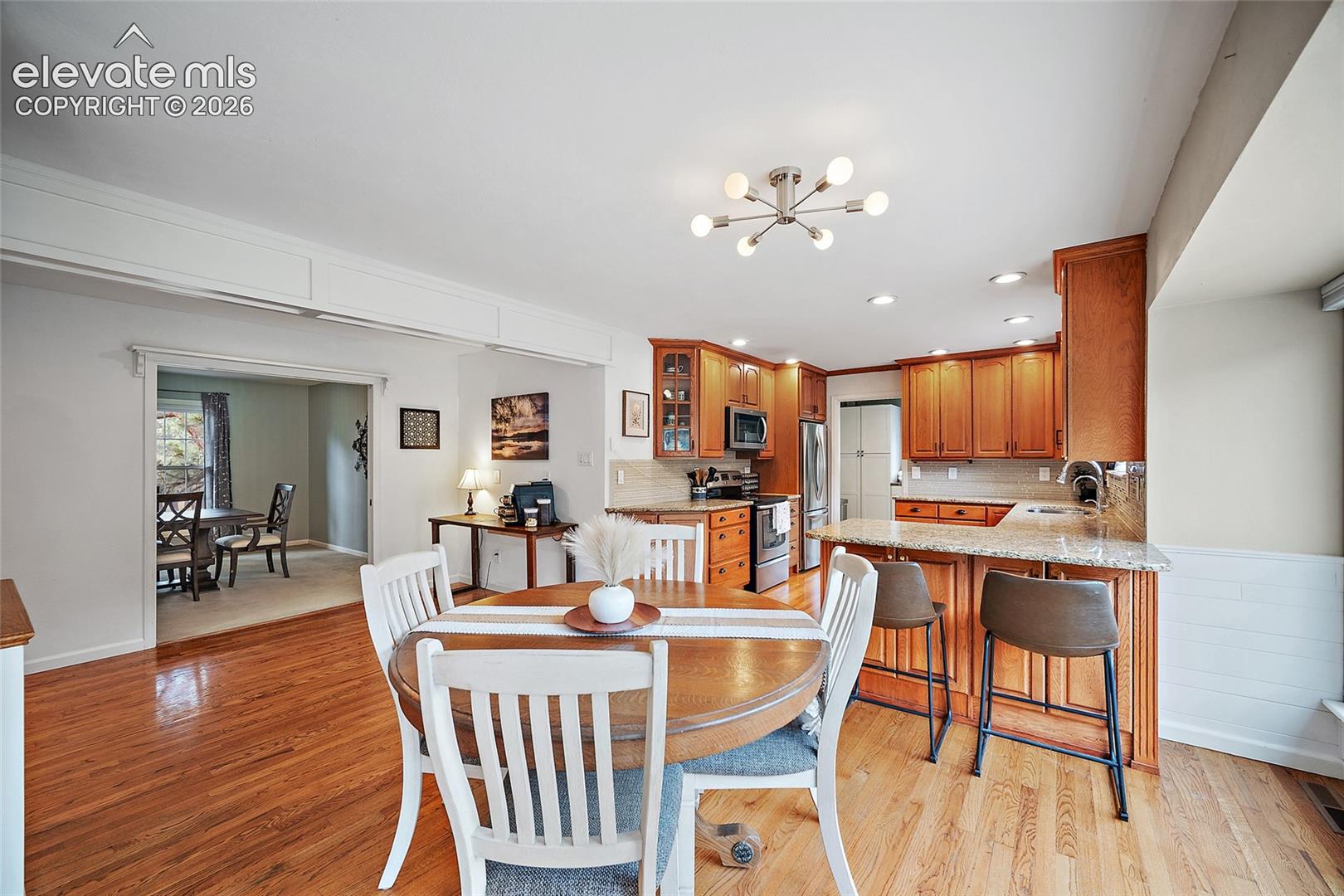 Kitchen featuring wood cabinetry, stone-finish countertops, stainless steel appliances, a multi-bulb light fixture, and wood-finish flooring