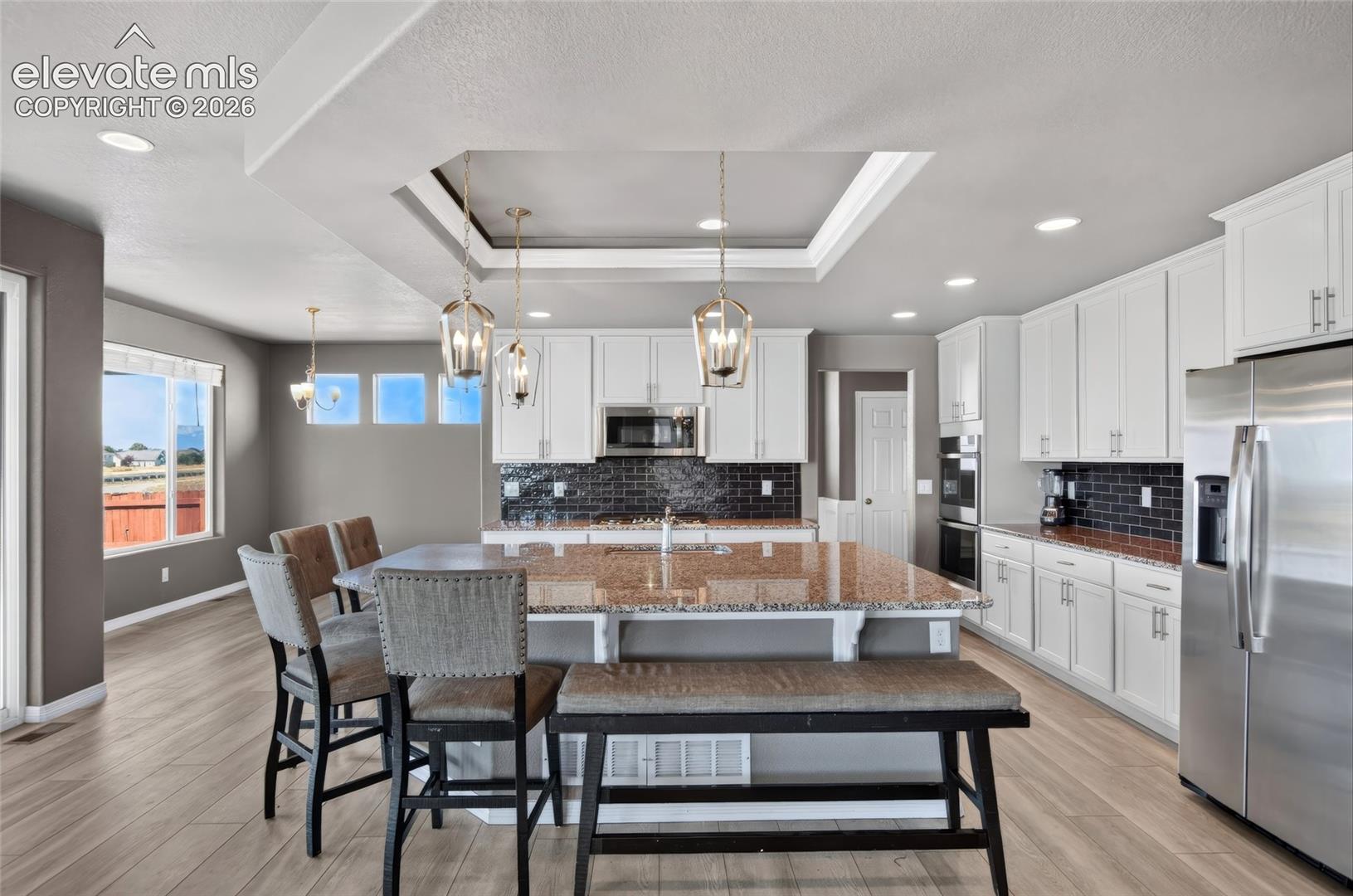 Kitchen featuring a central island with a granite countertop, white cabinetry with contemporary hardware, stainless steel appliances, a subway tile backsplash, and wood-finish flooring