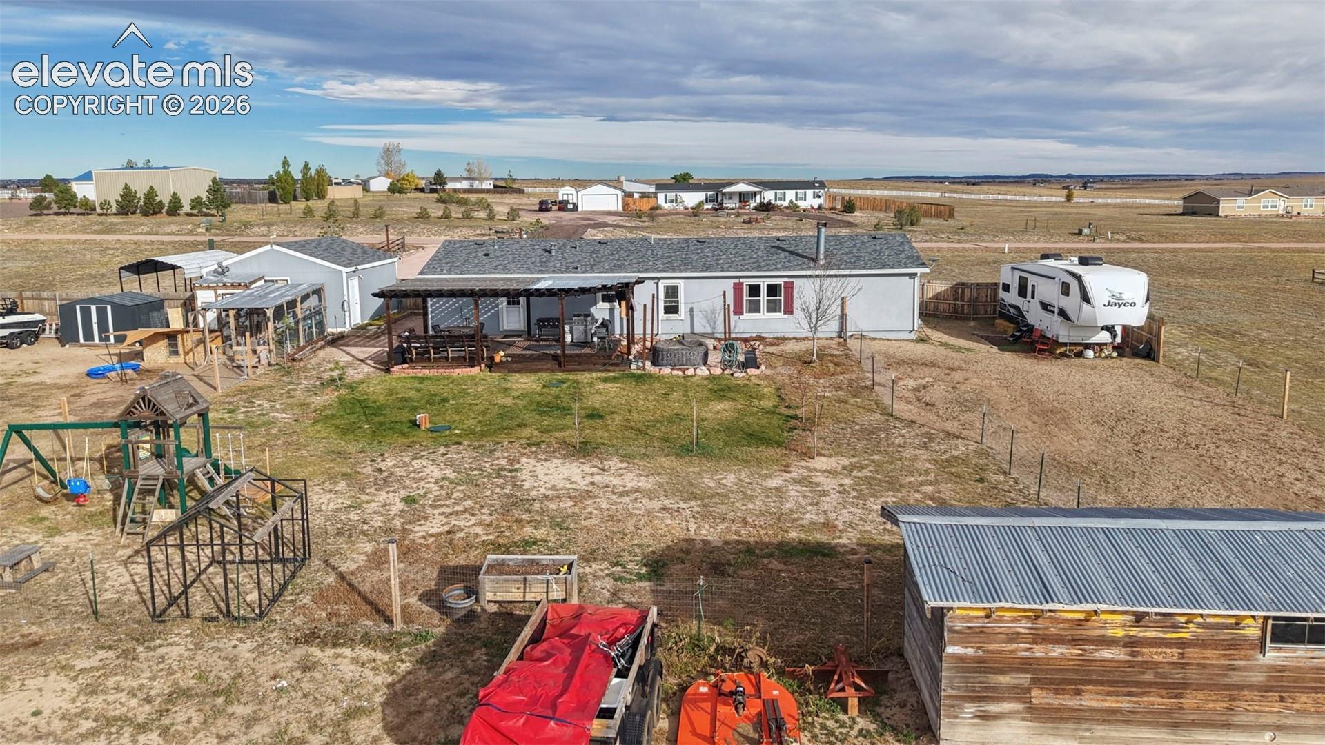 Expansive acreage featuring a covered patio with pergola, multi-purpose outbuildings, and perimeter fencing