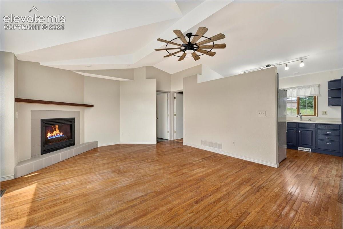 Vaulted ceiling with a multi-blade ceiling fan, wood-finish flooring, and a fireplace featuring a tile surround and a wood mantel