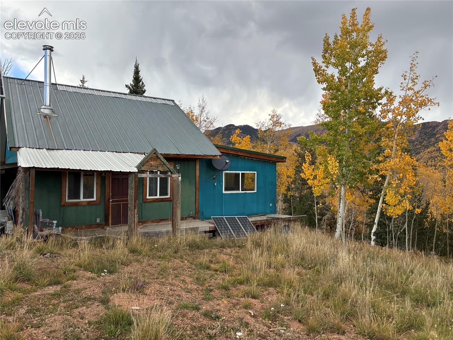 Exterior featuring a metal roof, metal chimney flue, wooden deck, solar panel installation, and mountain backdrop