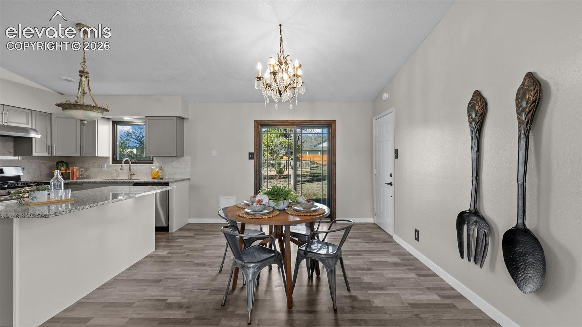 Kitchen featuring stone countertops, cabinetry with silver-toned hardware, wood-finish flooring, a tiered crystal chandelier, and sliding glass doors
