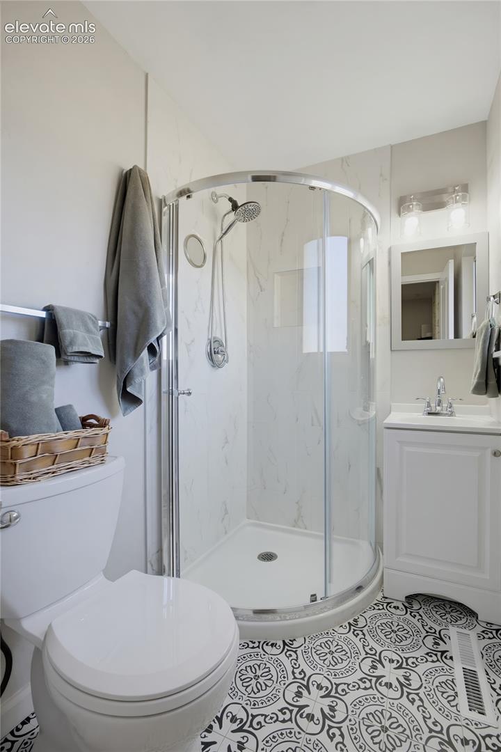 Walk-in shower with curved glass enclosure, white vanity with integrated sink, patterned floor tile, and wall-mounted mirror