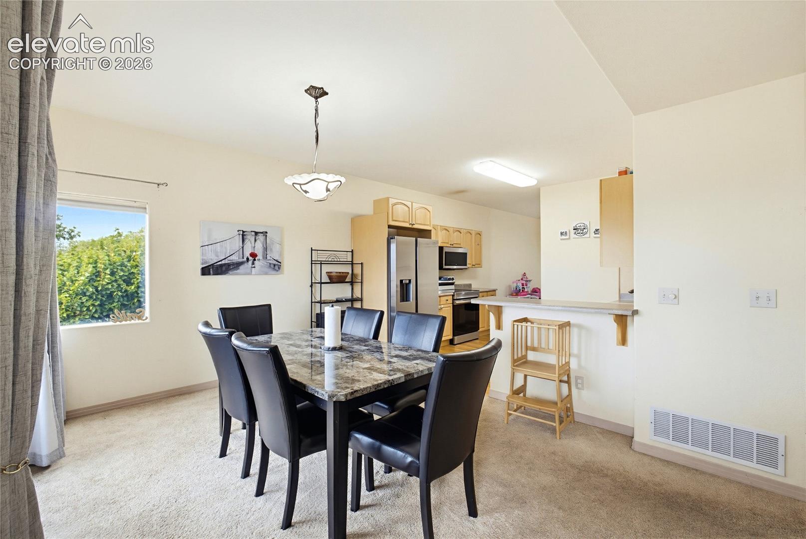 Open-concept dining area with a contemporary chandelier, carpeted flooring, and a window providing natural light