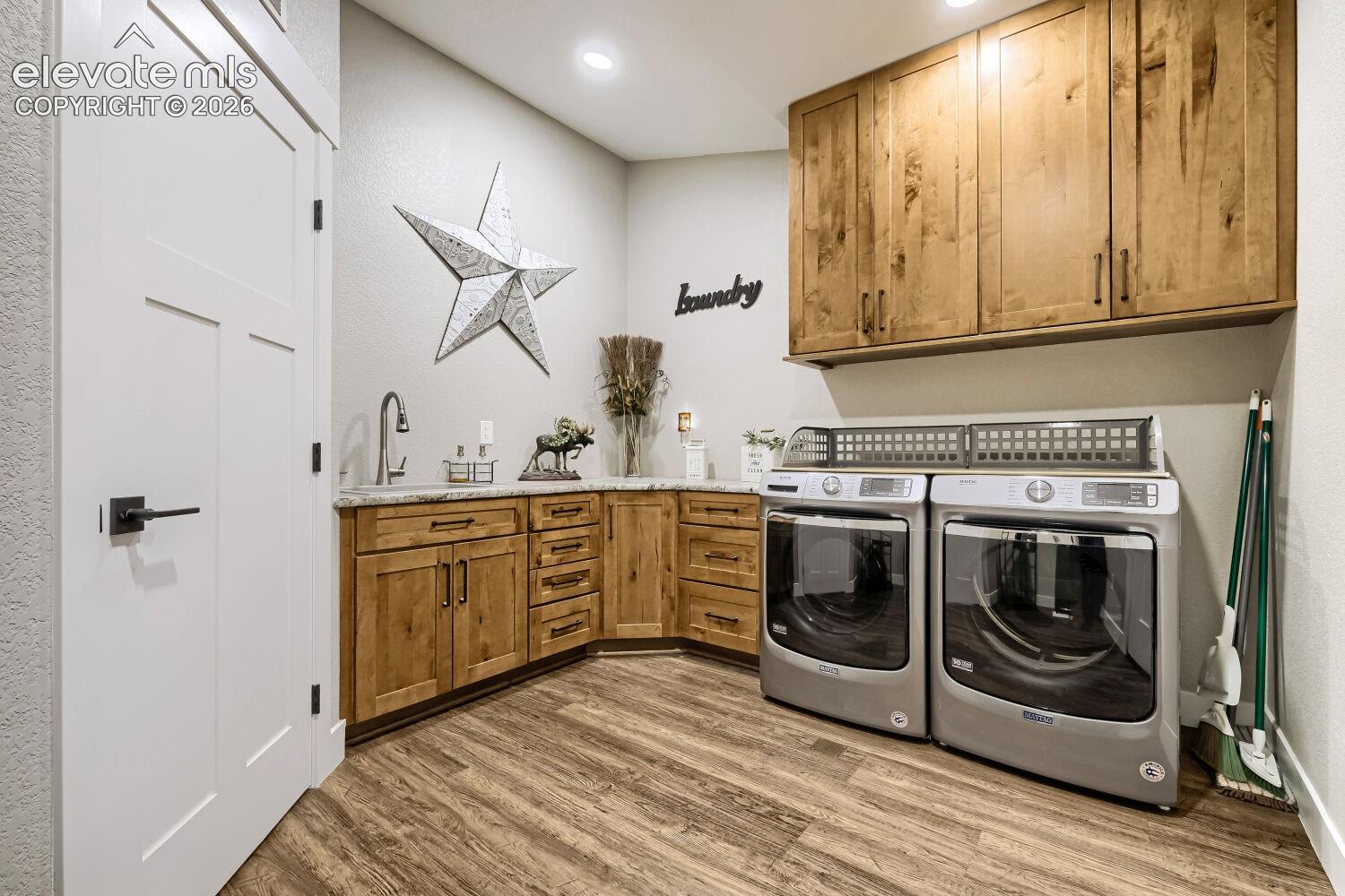Wood-finish flooring with a multi-panel interior door, base cabinetry with a countertop and sink, and upper wood-finish cabinetry