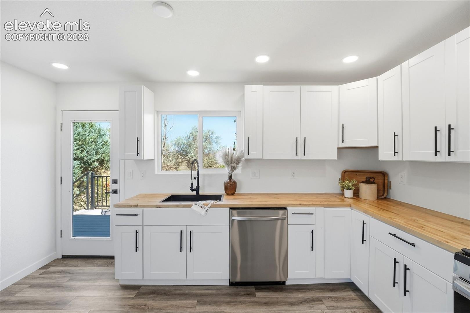 Kitchen featuring white shaker cabinetry, wood-finish countertops, stainless steel dishwasher, and a black single-basin sink with a matte black faucet