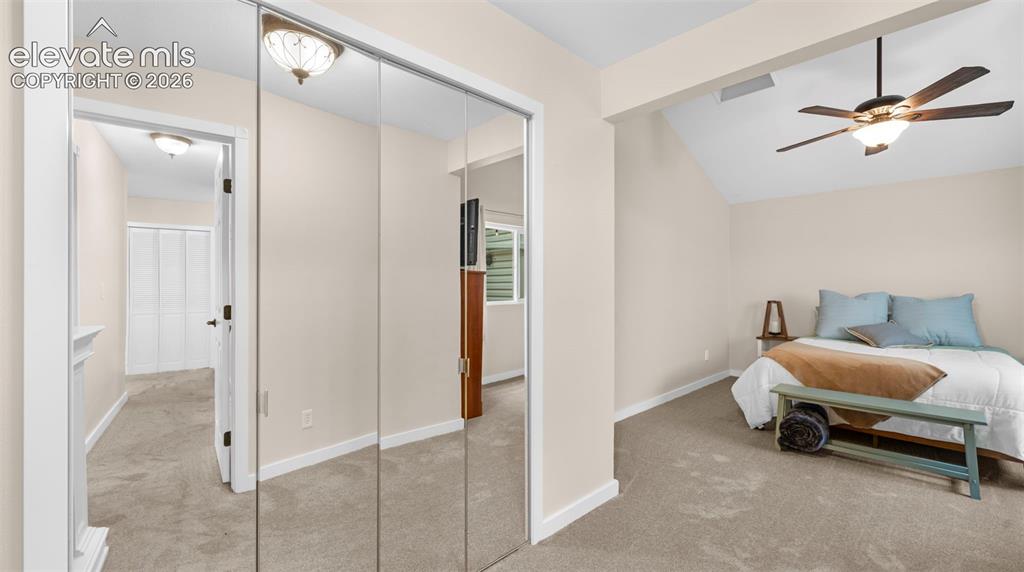 Carpeted interior space featuring mirrored closet doors, a vaulted ceiling, and a ceiling fan with integrated lighting