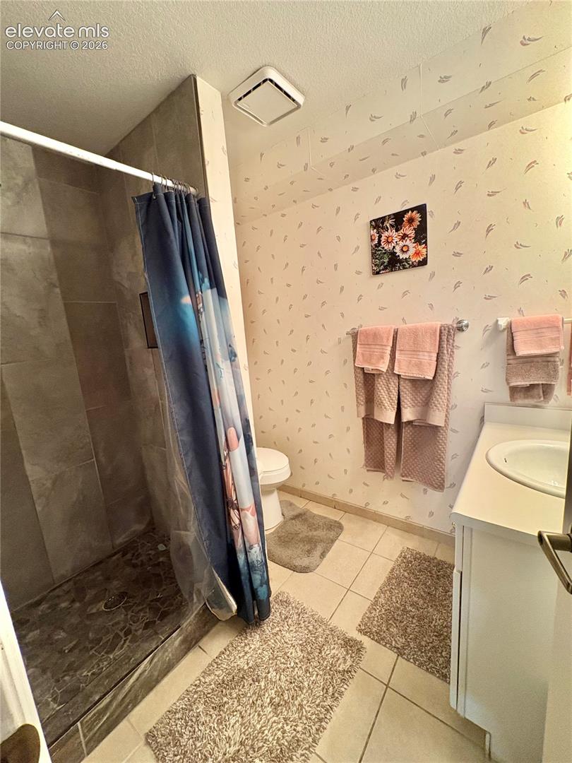 Tiled flooring with a walk-in shower, a single vanity with an integrated sink, and white cabinetry