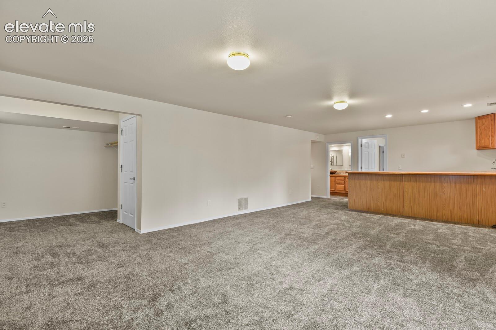 Open-concept interior featuring wall-to-wall carpeting, flush-mount ceiling lighting, a built-in wood-finish breakfast bar, and an enclosed reach-in closet