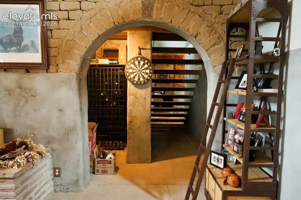 Stone archway entrance featuring a visible wine rack behind a metal gate, open-tread staircase, and a tall metal and wood-finish shelving unit
