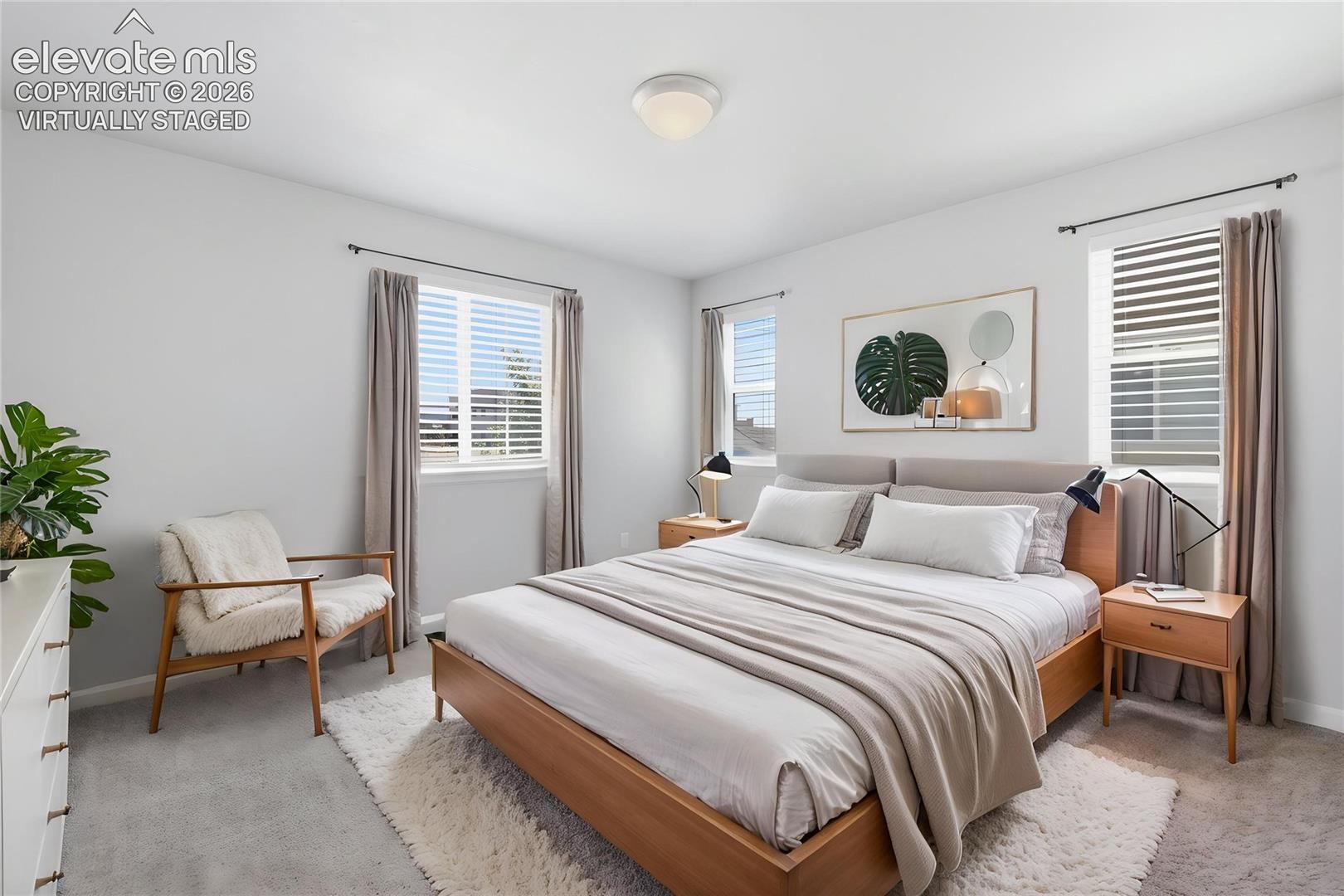 Primary bedroom featuring multiple windows with blinds, a ceiling-mounted light fixture, and light-toned walls -- virtually staged.