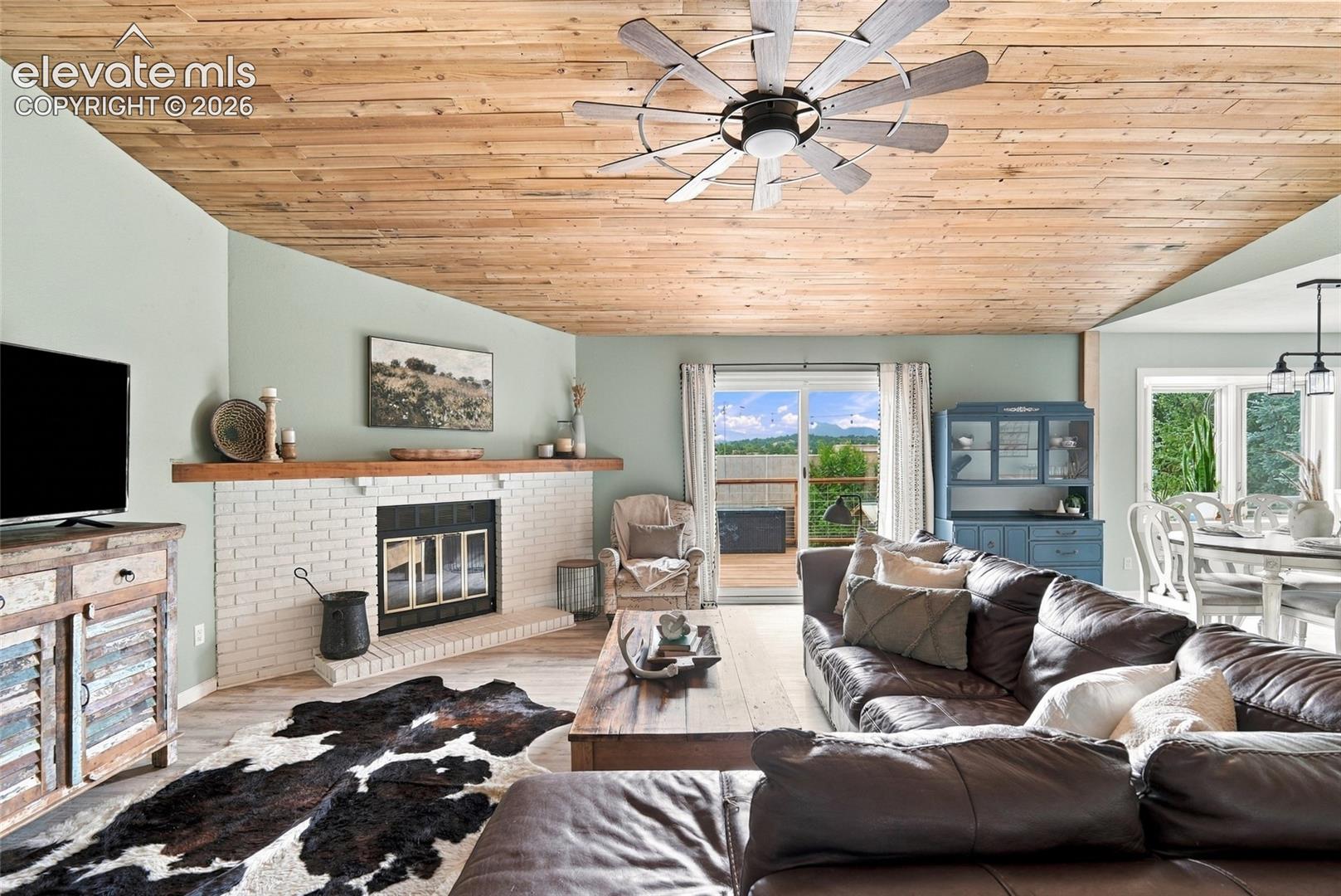 Vaulted wood-finish ceiling, brick fireplace with wood mantel, and sliding glass door to an outdoor deck