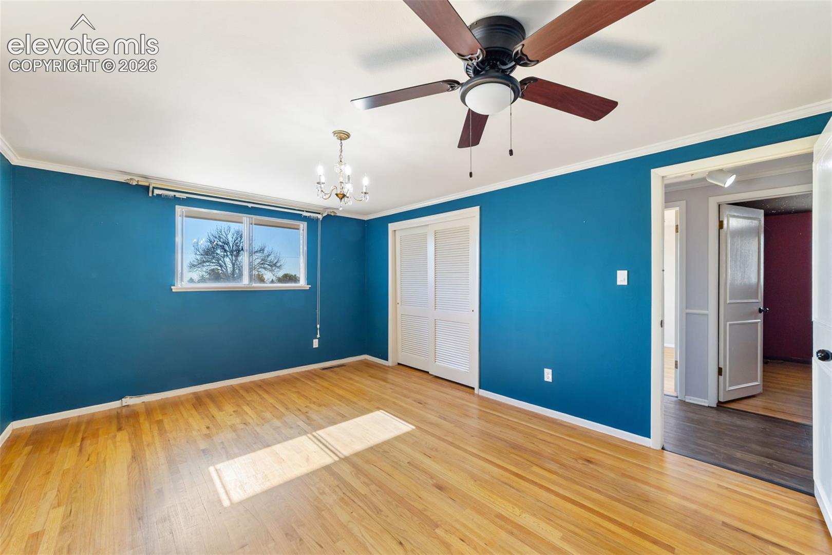 Hardwood flooring throughout featuring white baseboards, a ceiling fan with integrated lighting, and a traditional chandelier