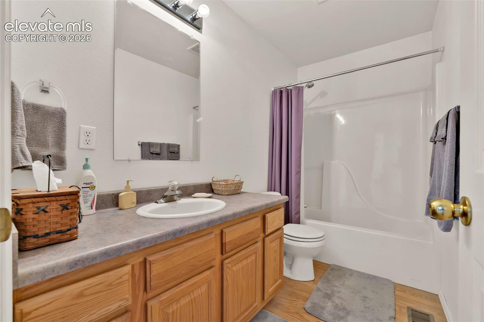 Bathroom featuring a single vanity with wood-finish cabinetry, a built-in sink, and a shower-tub combination