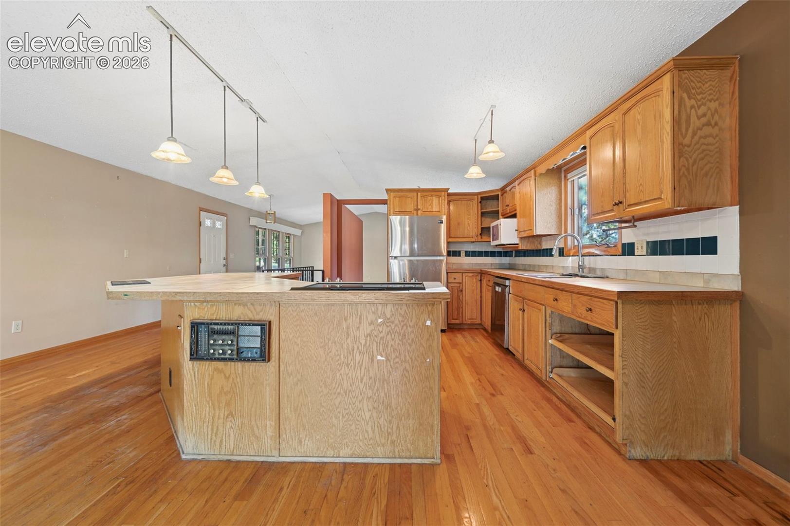 Kitchen featuring wood-finish flooring, wood cabinetry, recessed lighting, track lighting, and a stainless steel refrigerator