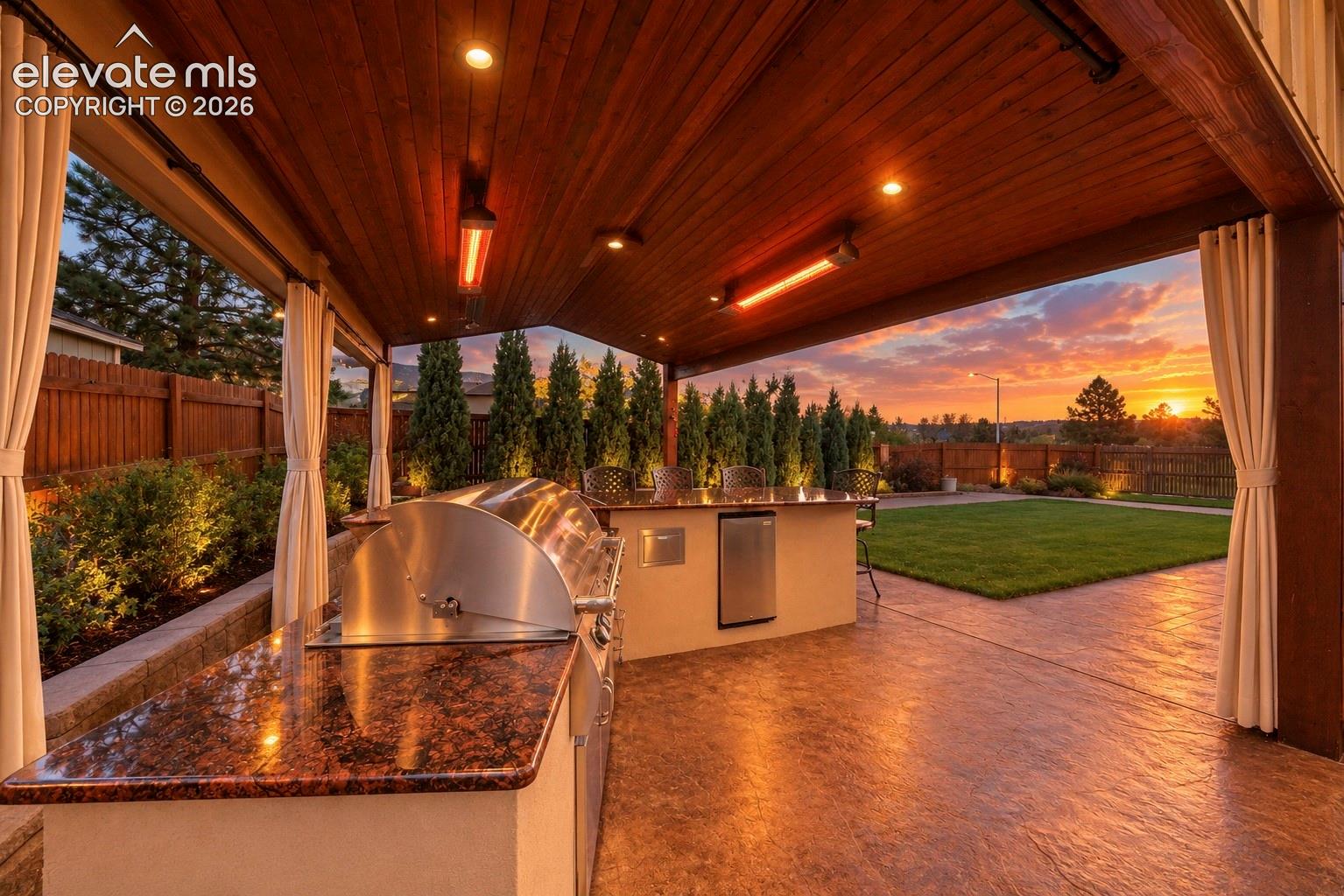 Covered outdoor kitchen featuring a stone-finish countertop, built-in stainless steel grill, integrated under-counter refrigeration, recessed ceiling lighting, and a wood-paneled ceiling